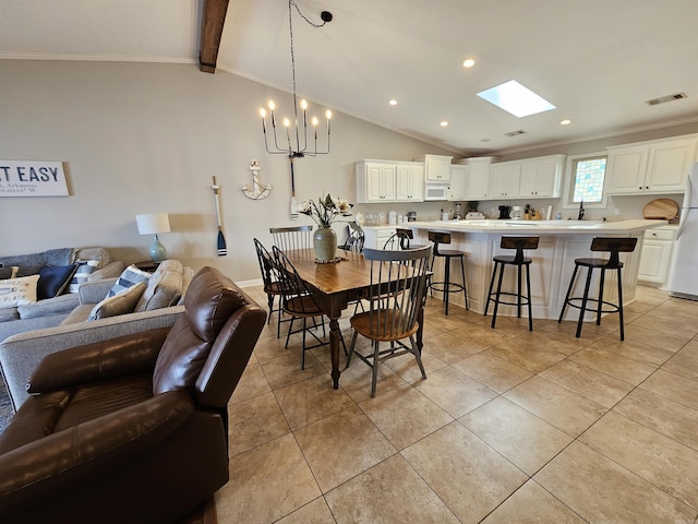 tiled dining room with sink, vaulted ceiling with skylight, crown molding, and a notable chandelier