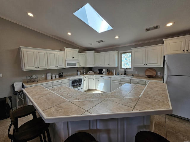 kitchen with a breakfast bar, white appliances, sink, white cabinets, and tile counters