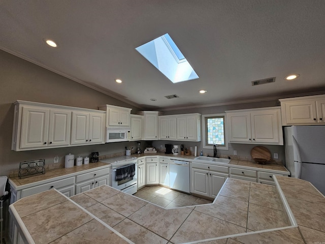 kitchen with vaulted ceiling with skylight, white appliances, sink, tile countertops, and white cabinetry