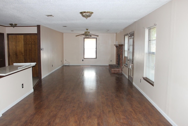 unfurnished living room featuring a textured ceiling, a brick fireplace, ceiling fan, and dark wood-type flooring