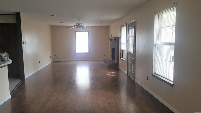 unfurnished living room featuring plenty of natural light, ceiling fan, dark hardwood / wood-style flooring, and a brick fireplace