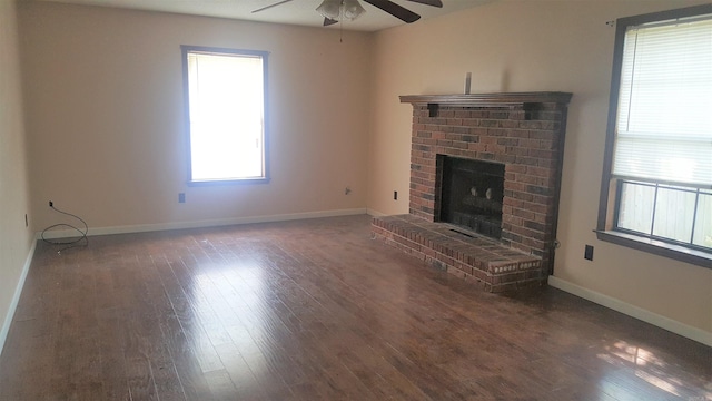 unfurnished living room with dark hardwood / wood-style flooring, ceiling fan, a fireplace, and a healthy amount of sunlight