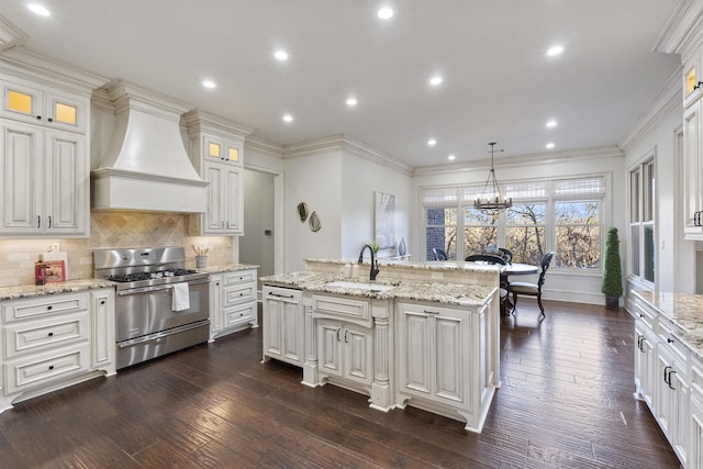 kitchen with tasteful backsplash, custom range hood, gas stove, sink, and pendant lighting