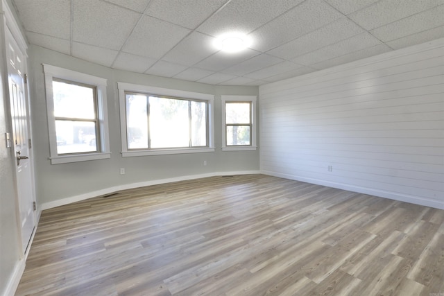 spare room with wood walls, a drop ceiling, and light hardwood / wood-style floors