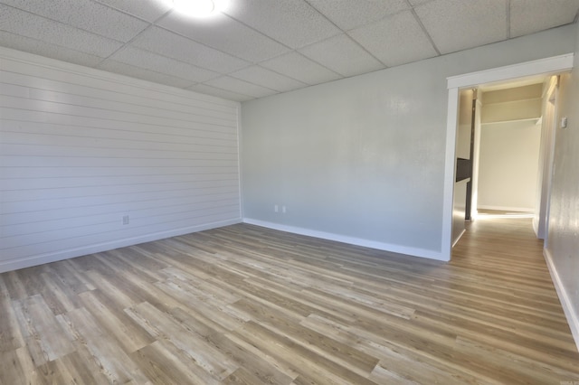 spare room with a paneled ceiling, wooden walls, and light wood-type flooring