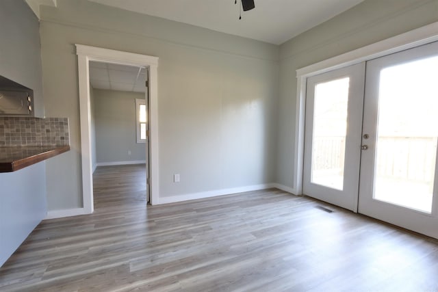 unfurnished dining area with ceiling fan, french doors, and light hardwood / wood-style floors