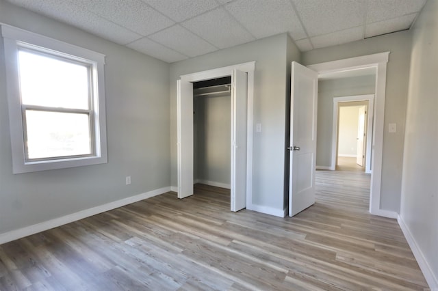 unfurnished bedroom with a paneled ceiling, a closet, and light hardwood / wood-style flooring