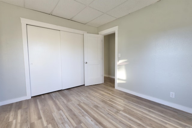 unfurnished bedroom with a paneled ceiling, light hardwood / wood-style floors, and a closet