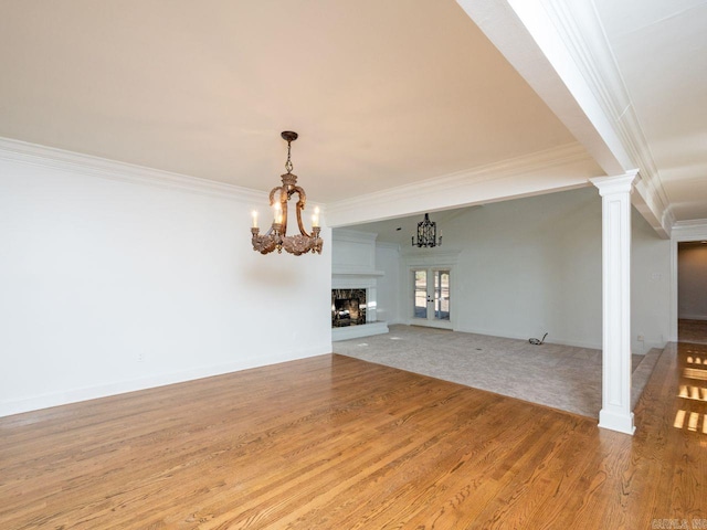 unfurnished living room with french doors, a notable chandelier, decorative columns, crown molding, and light hardwood / wood-style floors