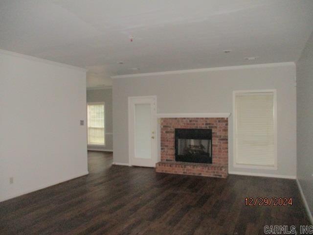 unfurnished living room featuring dark hardwood / wood-style floors, crown molding, and a brick fireplace