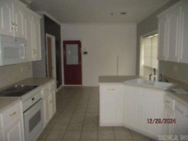 kitchen with white cabinetry, sink, light tile patterned flooring, and white appliances