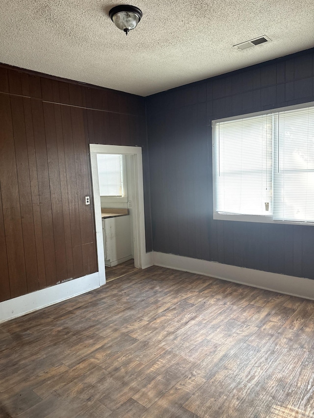 spare room featuring a textured ceiling, wood walls, and dark wood-type flooring