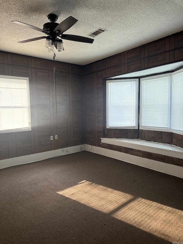 carpeted spare room with ceiling fan, a textured ceiling, and wooden walls