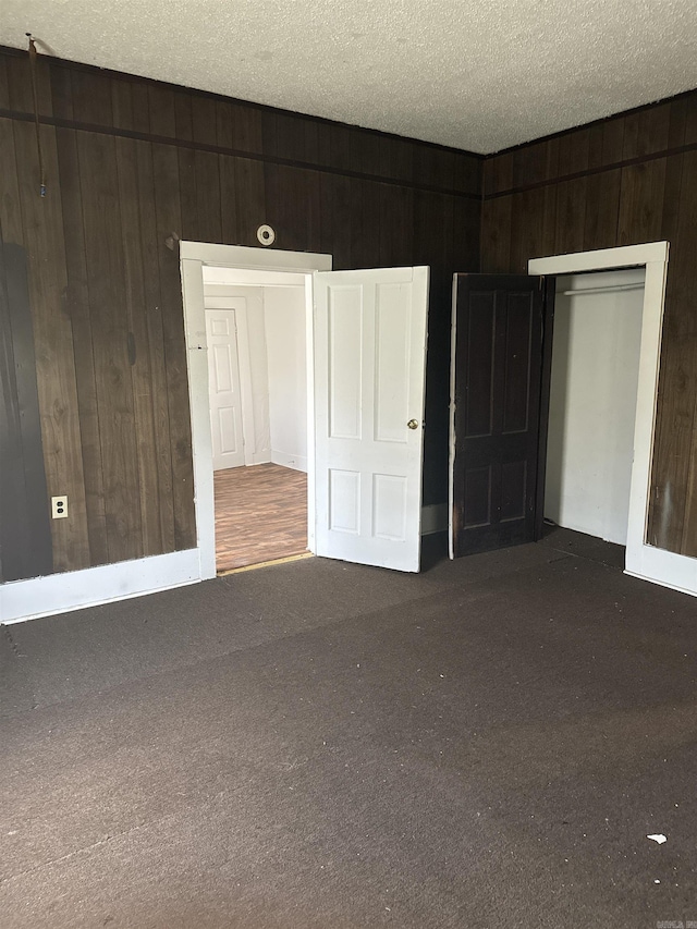 unfurnished bedroom with carpet, a textured ceiling, a closet, and wood walls