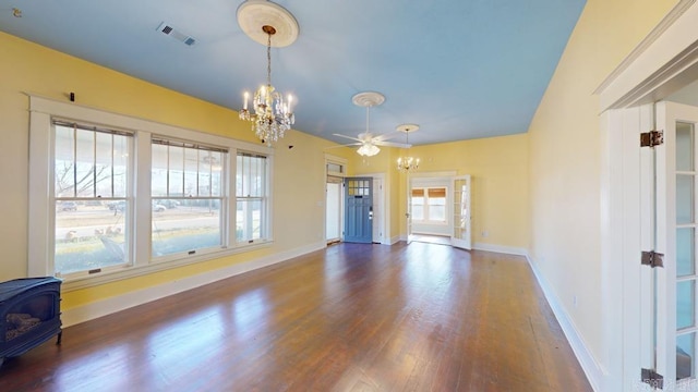 unfurnished living room featuring a wood stove, dark hardwood / wood-style floors, and ceiling fan with notable chandelier