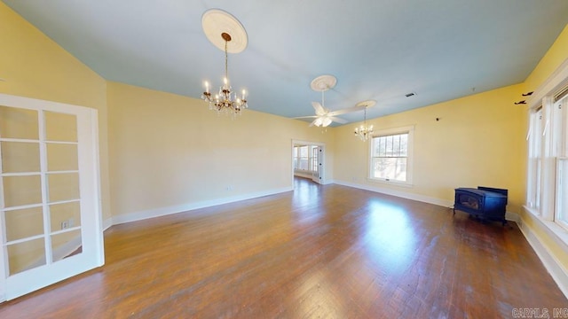 empty room with a wood stove, wood-type flooring, and ceiling fan with notable chandelier