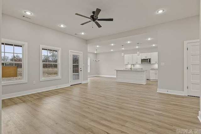 unfurnished living room featuring ceiling fan with notable chandelier and light hardwood / wood-style floors