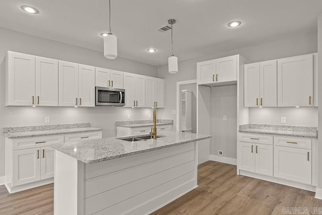 kitchen featuring sink, white cabinets, an island with sink, and decorative light fixtures