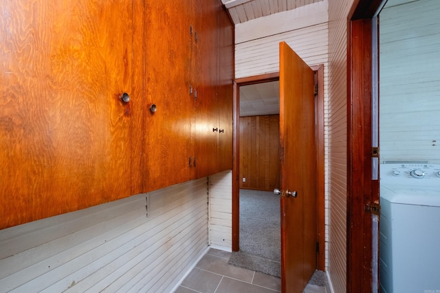 hallway featuring tile patterned flooring, wood walls, and washer / dryer