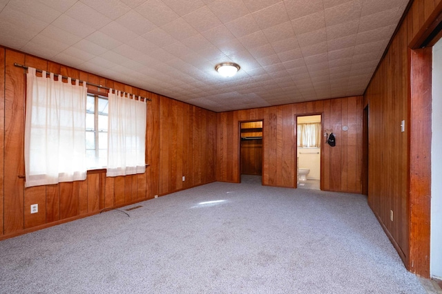 unfurnished bedroom featuring wood walls, light colored carpet, and connected bathroom