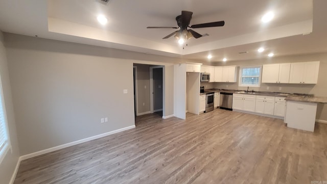 kitchen featuring appliances with stainless steel finishes, a tray ceiling, sink, light hardwood / wood-style floors, and white cabinetry