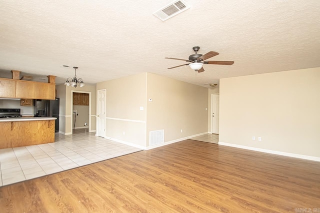 kitchen with pendant lighting, ceiling fan with notable chandelier, black fridge, light wood-type flooring, and a textured ceiling