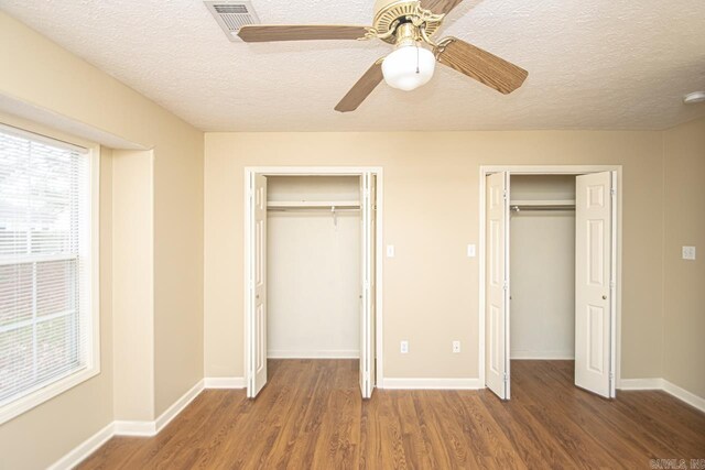 unfurnished bedroom featuring multiple closets, ceiling fan, dark wood-type flooring, and a textured ceiling