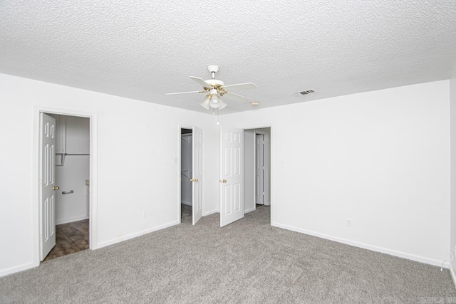 unfurnished bedroom featuring ceiling fan, a textured ceiling, a walk in closet, light carpet, and a closet