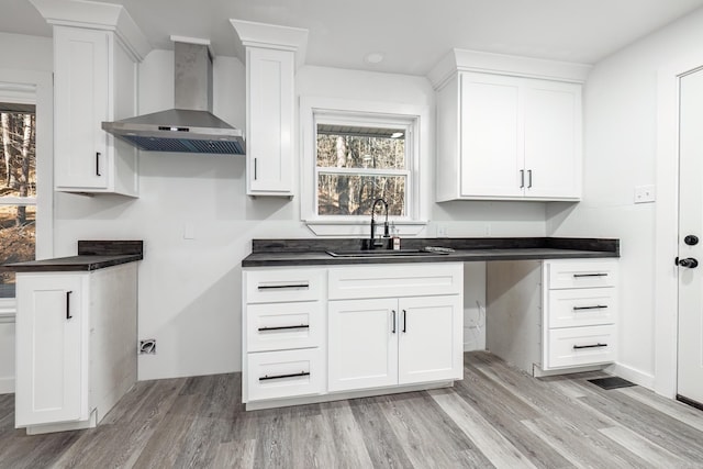 kitchen featuring white cabinetry, sink, wall chimney exhaust hood, and light wood-type flooring