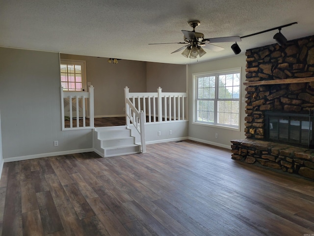 unfurnished living room with ceiling fan, rail lighting, dark wood-type flooring, a textured ceiling, and a fireplace