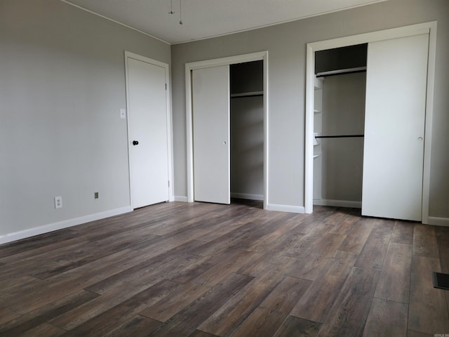 unfurnished bedroom featuring dark wood-type flooring and two closets