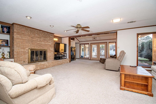 carpeted living room with a textured ceiling, ceiling fan, crown molding, and a fireplace