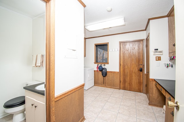 interior space featuring a textured ceiling, washer / dryer, crown molding, and wooden walls