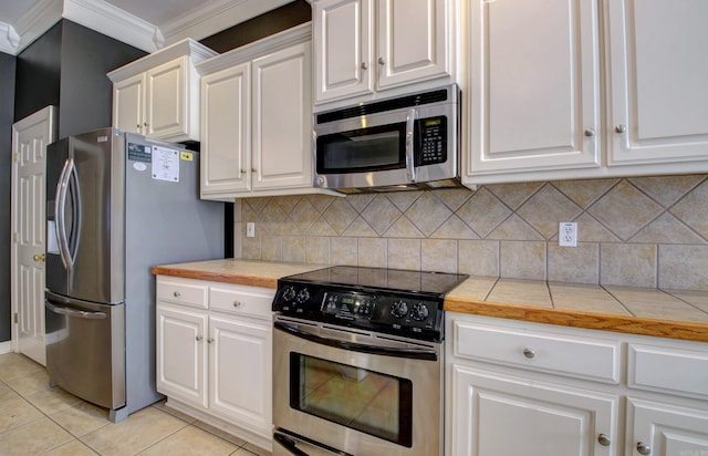 kitchen with tile countertops, ornamental molding, light tile patterned flooring, white cabinetry, and stainless steel appliances