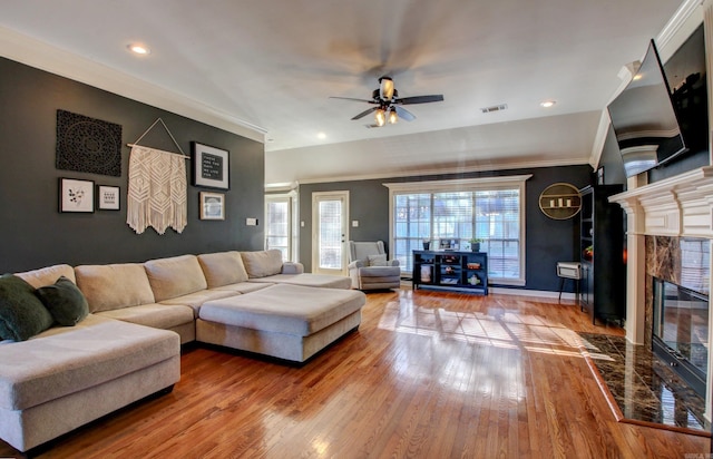 living room featuring hardwood / wood-style floors, ceiling fan, ornamental molding, and a premium fireplace