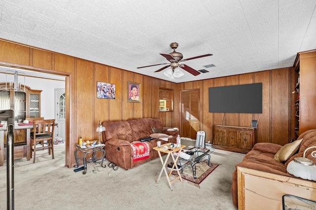 living room with ceiling fan, wood walls, and light colored carpet