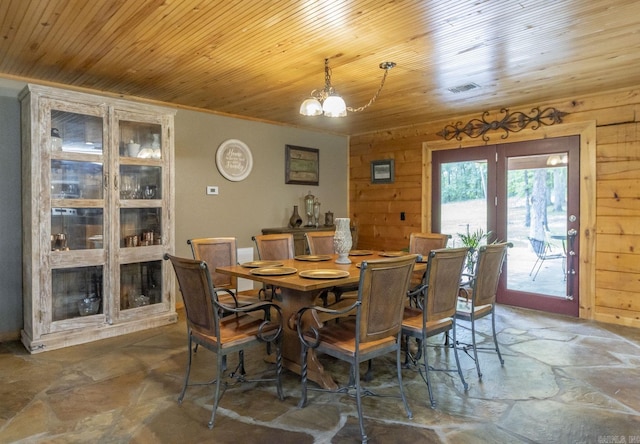 dining space with wood walls, wooden ceiling, crown molding, and an inviting chandelier