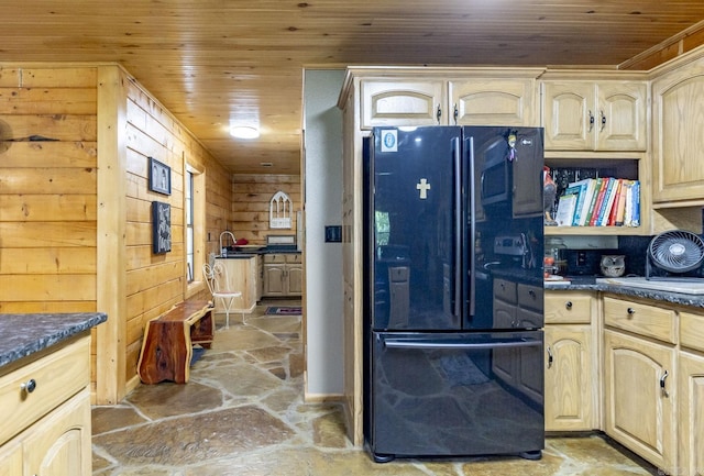 kitchen with light brown cabinetry, black fridge, wooden ceiling, and wood walls