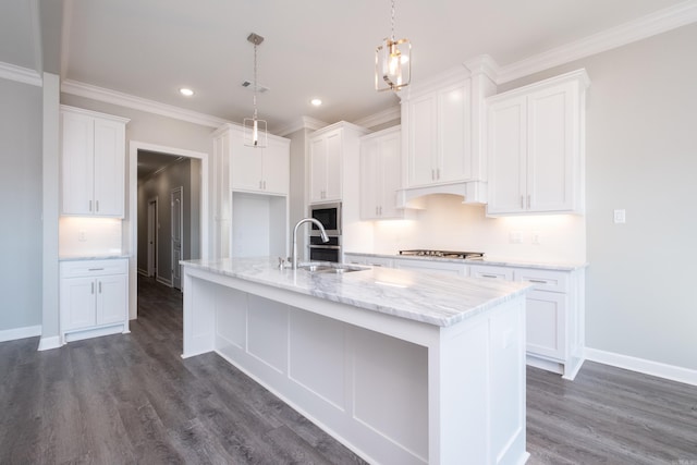 kitchen with built in microwave, sink, white cabinetry, hanging light fixtures, and an island with sink