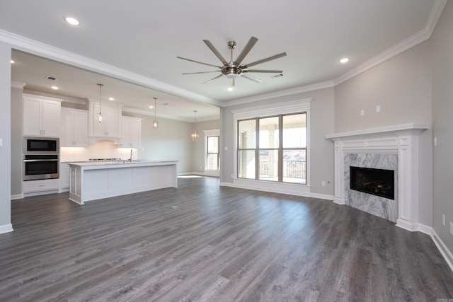 unfurnished living room with a premium fireplace, crown molding, ceiling fan, and dark wood-type flooring