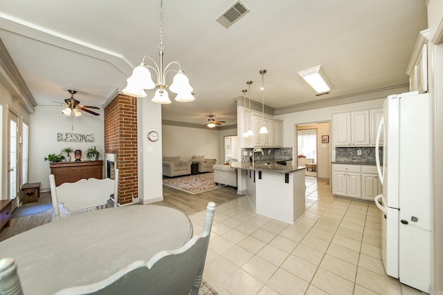 kitchen with tasteful backsplash, kitchen peninsula, white fridge, decorative light fixtures, and a breakfast bar