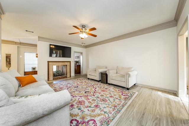 living room featuring light wood-type flooring, ceiling fan, crown molding, and a tiled fireplace