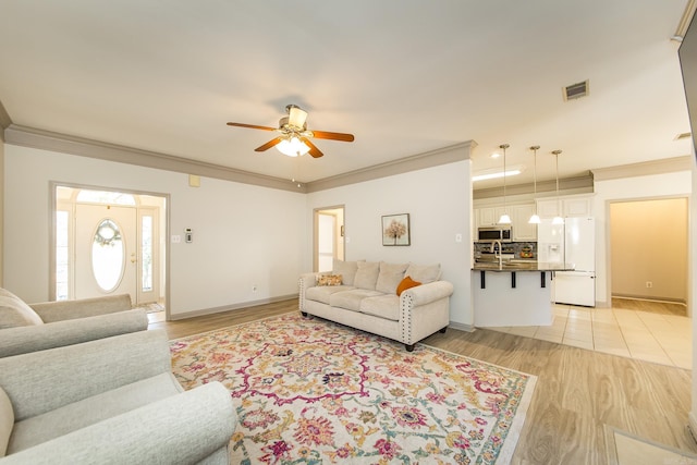 living room featuring light hardwood / wood-style flooring, ceiling fan, crown molding, and sink