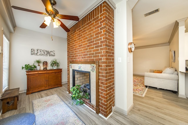 living room featuring ceiling fan, a brick fireplace, light wood-type flooring, vaulted ceiling, and ornamental molding