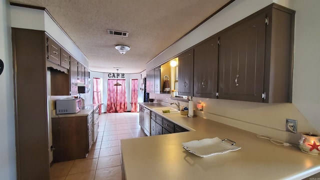 kitchen featuring sink, kitchen peninsula, a textured ceiling, dark brown cabinets, and light tile patterned floors