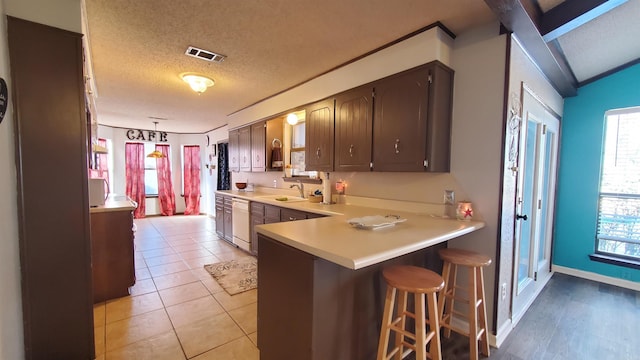 kitchen with kitchen peninsula, a breakfast bar, a textured ceiling, dishwasher, and light tile patterned flooring