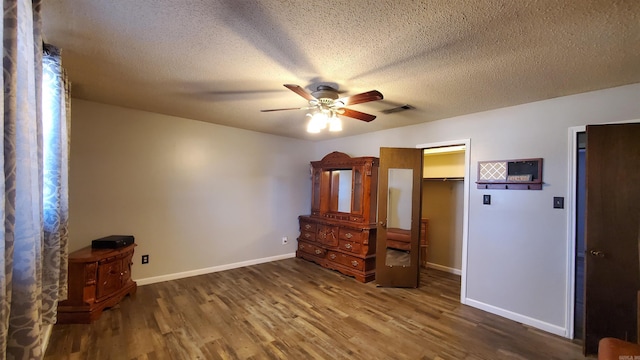 unfurnished bedroom featuring ceiling fan, a spacious closet, dark wood-type flooring, a textured ceiling, and a closet