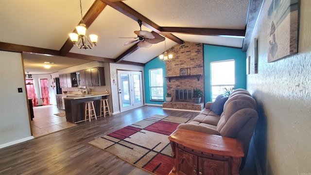 living room with vaulted ceiling with beams, dark wood-type flooring, ceiling fan with notable chandelier, and a brick fireplace