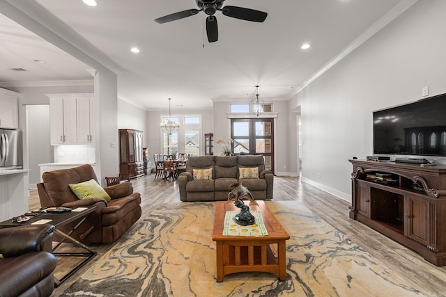 living room with ornamental molding, ceiling fan with notable chandelier, and light wood-type flooring