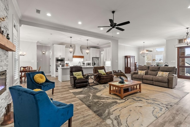 living room featuring ceiling fan with notable chandelier, light hardwood / wood-style floors, crown molding, and a fireplace